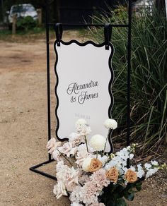 a sign that is sitting in the dirt with flowers next to it and some grass