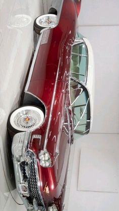 an old red car is parked in the corner of a white room with tile flooring