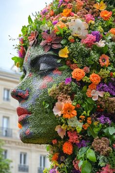 a woman's face covered in flowers and greenery next to a tall building