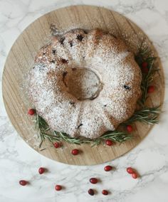 a bundt cake with powdered sugar and cranberries on a wooden platter