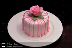 a pink and white striped cake with a single rose on top sitting on a plate