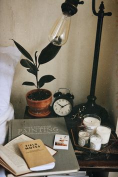 a table with books, candles and an alarm clock on it next to a lamp