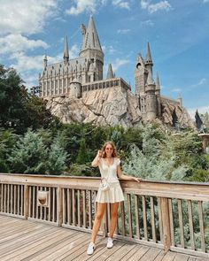 a woman standing on top of a wooden bridge next to hogwart's castle