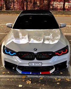 the front end of a white bmw car parked in a parking lot with its lights on