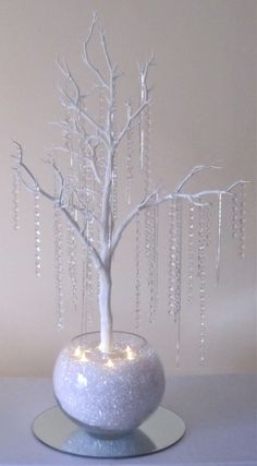 a white tree in a glass vase with lights on the branches and beads hanging from it