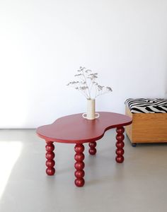 a red table sitting next to a white wall with a vase on top of it