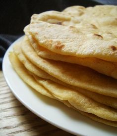 stack of tortillas sitting on top of a white plate next to a wooden table