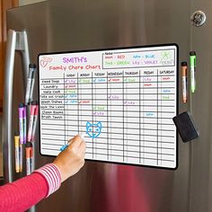 a child is writing on a white board in front of a stainless steel freezer