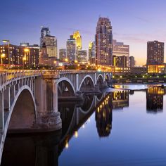 the city skyline is lit up at night with lights reflecting in the water and bridge