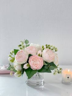 a vase filled with pink and white flowers next to a candle