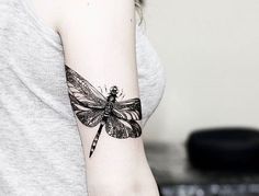 a woman's arm with a dragonfly tattoo on the left side of her arm