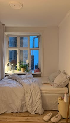 a bed room with a neatly made bed next to a window and a plant in the corner