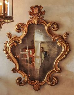 an ornate mirror hanging on the wall next to a light fixture and candle holder in a room