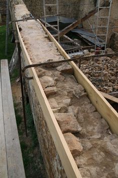 a wooden bench sitting in front of a stone wall and some scaffolds