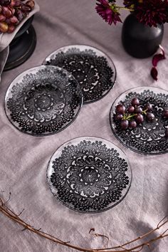 three black and white plates sitting on top of a table covered in grapes next to a vase