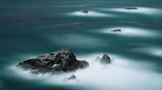 some rocks in the water and one is on top of it with waves coming up