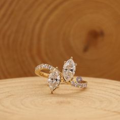 an engagement ring with two pear shaped diamonds on it, sitting on top of a piece of wood