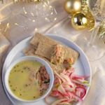 a white plate topped with soup and veggies next to crackers on a table