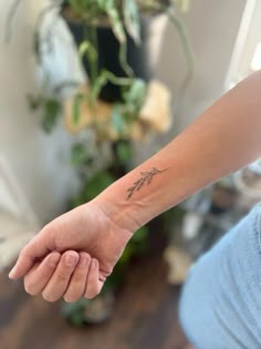 a woman's arm with a small tattoo on it, in front of a plant