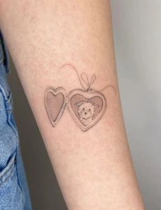 a small tattoo with two hearts and a teddy bear in the middle on the arm