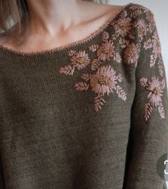 a woman wearing a brown sweater with pink flowers on the front and side, standing in front of a white wall