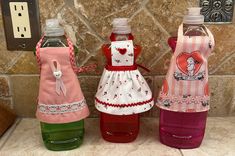 three plastic bottles with aprons on them sitting next to each other in front of a stone wall