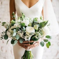 a bride holding a bouquet of white flowers and greenery