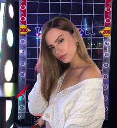 a woman with long hair posing in front of a tv screen wearing a white sweater