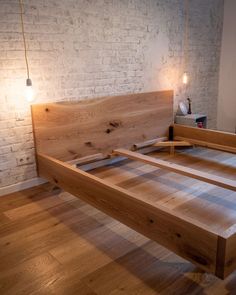 a wooden bed frame sitting on top of a hard wood floor next to a brick wall