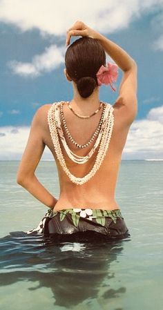 a woman in the ocean wearing pearls and necklaces on her back, looking at the water