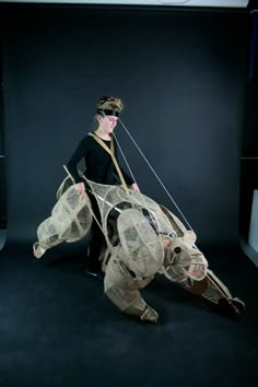 a woman is standing in front of a black background holding an animal made out of newspaper