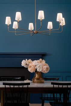 a chandelier hanging over a dining room table with flowers in the vase on it