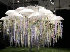 several white umbrellas hanging from the ceiling in front of purple flowers and greenery