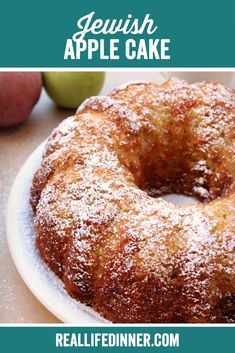 a cake sitting on top of a white plate next to two apples and a cup