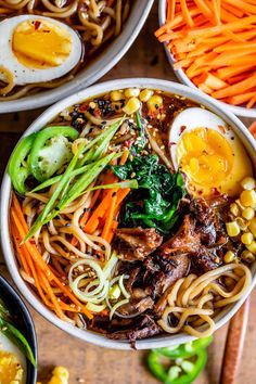 three bowls filled with noodles, carrots and an egg sitting on top of a wooden table