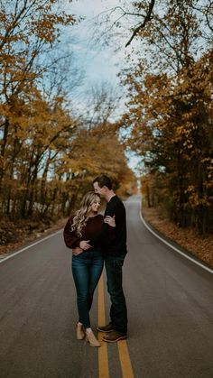 a man and woman standing on the side of an empty road with trees in the background