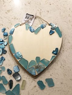 a heart shaped mirror sitting on top of a counter next to sea glass pieces and a tag