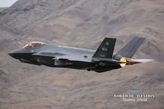 a fighter jet flying through the air with mountains in the background