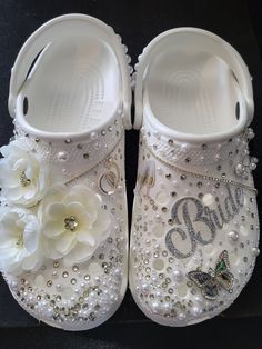 a pair of white baby shoes with flowers and pearls on the bottom one shoe has a butterfly