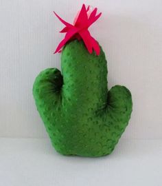 a green cactus with a pink flower on it's head sitting in front of a white wall