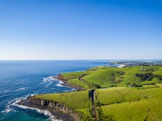 an aerial view of the ocean and green fields near some cliffs with houses on them