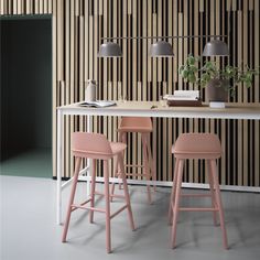 three pink stools in front of a white table with black and brown striped wallpaper