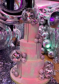 a three tiered cake with disco balls on top and silver confetti around it