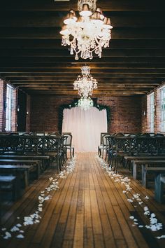 the aisle is decorated with white flowers and chandelier hanging from the brick ceiling