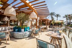 an outdoor seating area with tables and chairs, blue cushions and palm trees in the background