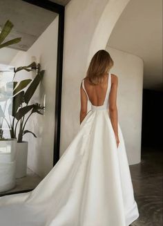 a woman in a white wedding dress is looking at herself in the mirror and she has her back turned to the camera