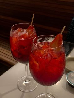 two glasses filled with red liquid and strawberries on top of a white tablecloth