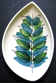 a white plate with green leaves painted on the inside of it, sitting on a black surface