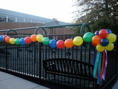 balloons and streamers are tied to a fence near a park bench in front of a building