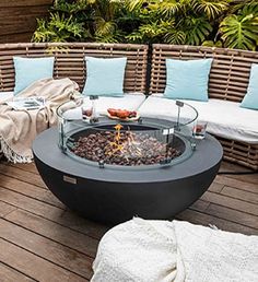 a fire pit sitting on top of a wooden deck next to couches and pillows